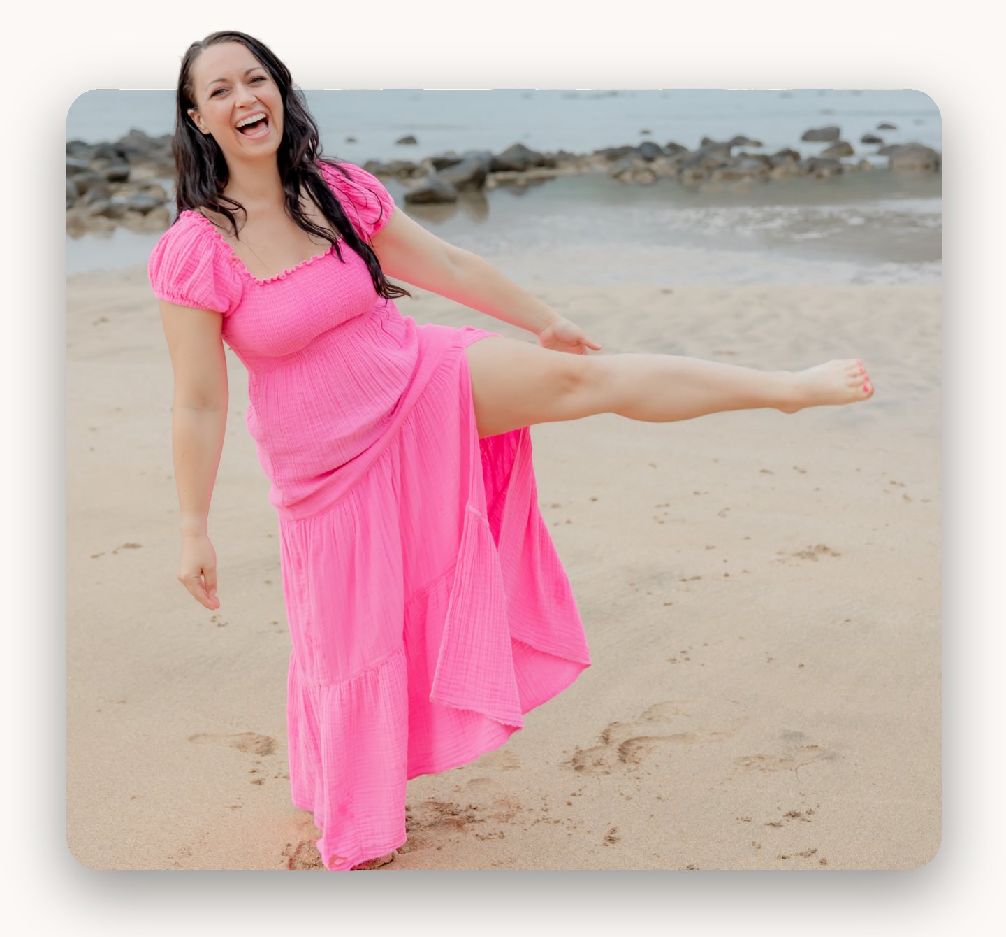 Amanda Monger laughing and kicking one leg up in a pink dress on a beach