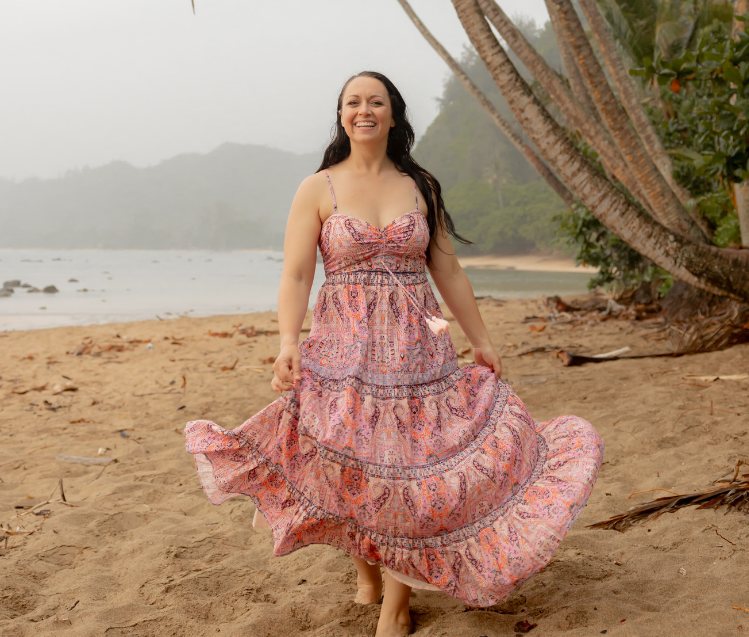Amanda twirling in a patterned dress on a beach under palm trees